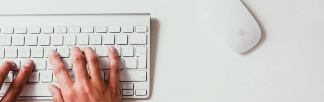Hands typing on a keyboard beside a computer mouse
